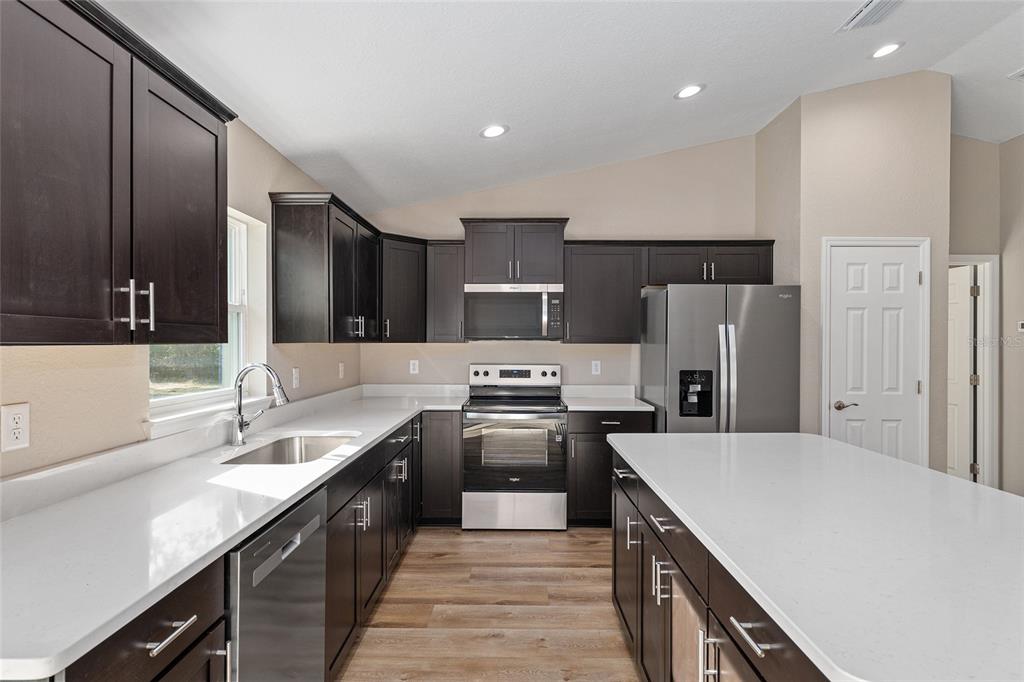 A kitchen features dark wood cabinets, white countertops, stainless steel appliances, and wood-look flooring — 8442 N TEMPEST DRIVE, CITRUS SPRINGS, FL
