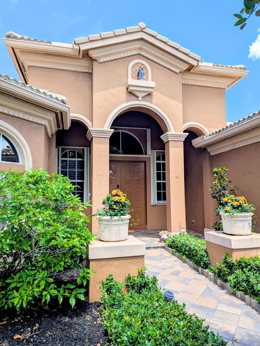 The exterior of a tan stucco house features an arched entryway with a stone walkway — 10640 Oak Meadow Lane, Lake Worth FL 33449, LAKE WORTH, FL