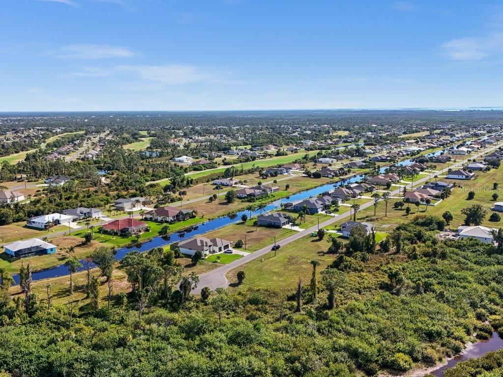 An aerial view shows a suburban neighborhood with houses lining a canal and surrounding vegetation — 176 W PINE VALLEY LANE, ROTONDA WEST, FL