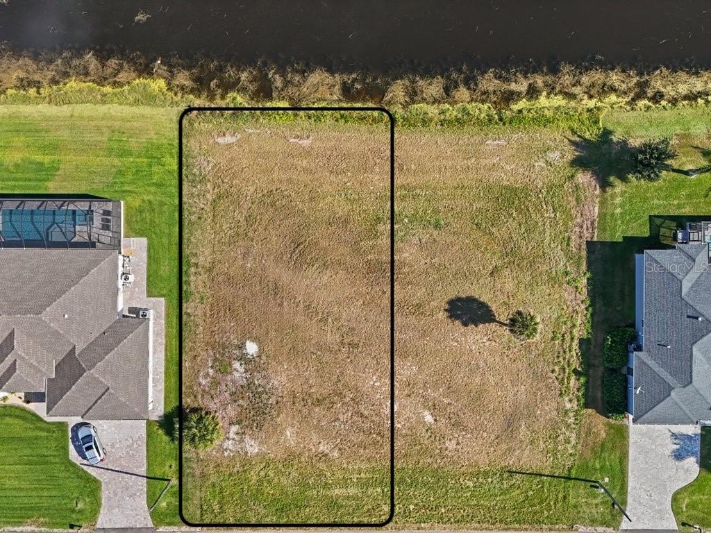 An aerial view shows a rectangular vacant lot situated between two houses near a canal — 176 W PINE VALLEY LANE, ROTONDA WEST, FL