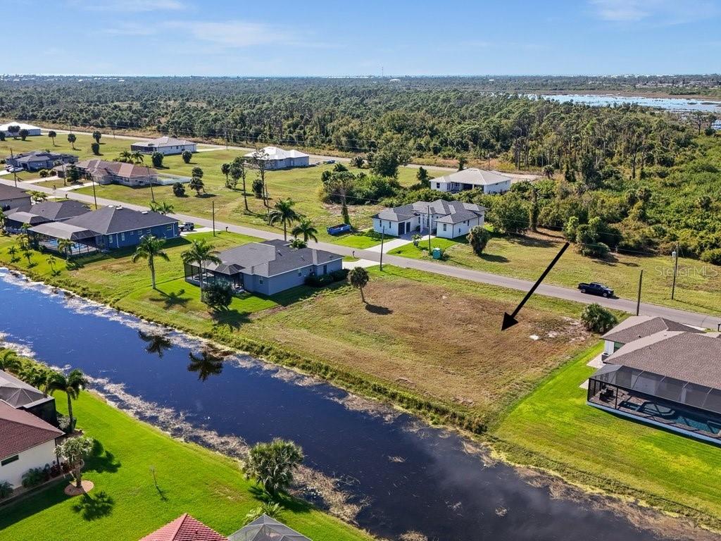 An aerial view shows a vacant, grassy residential lot situated next to a canal — 176 W PINE VALLEY LANE, ROTONDA WEST, FL