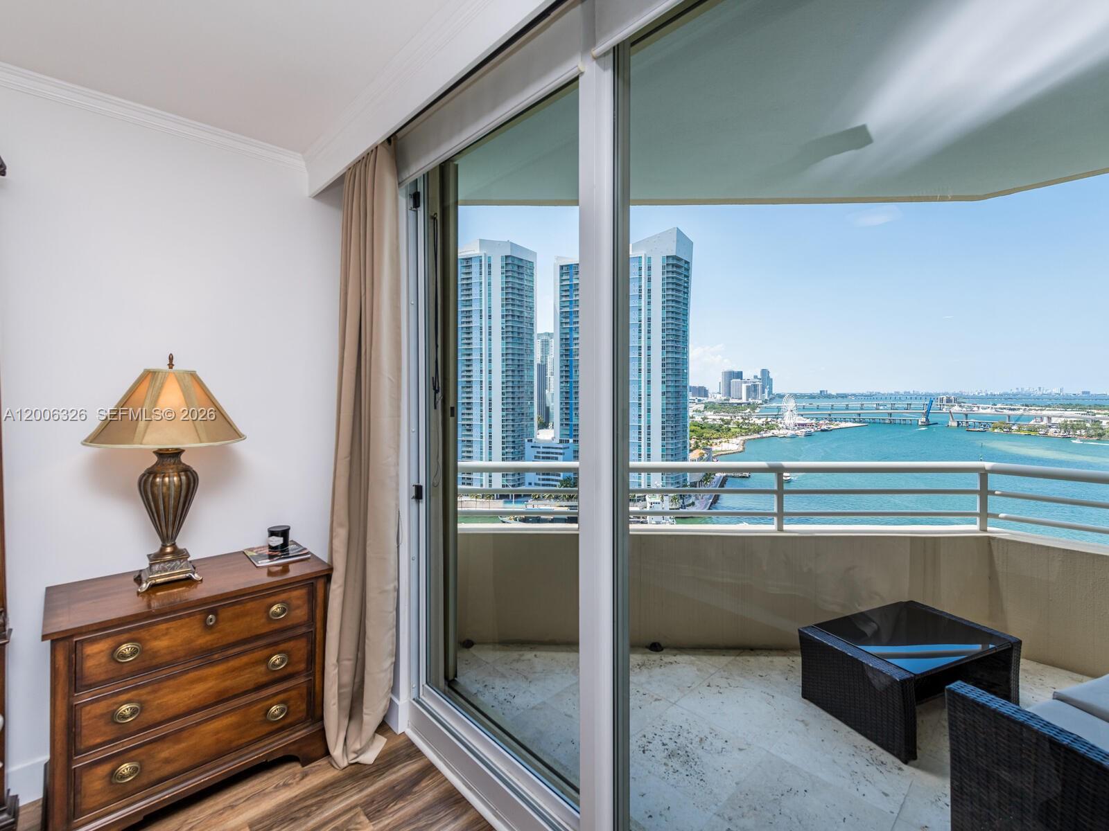 A bedroom with a wooden dresser and lamp opens onto a balcony overlooking the water — 888 Brickell Key Dr # 2112, Miami FL 33131, MIAMI, FL