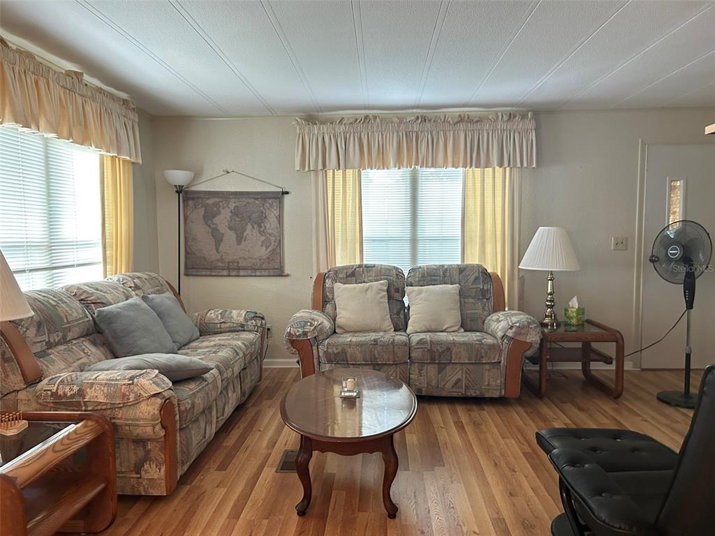 A living room features two patterned sofas, a wooden coffee table, and wood-look flooring — 8407 WEATHERFORD AVENUE, BROOKSVILLE, FL