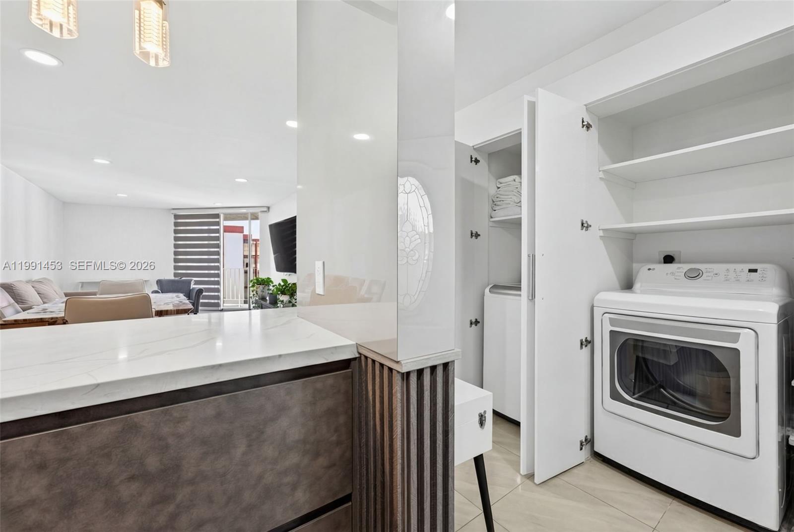 A laundry closet with a washer and dryer sits beside a kitchen counter and living area — 1750 W 46th St # 412, Hialeah FL 33012, HIALEAH, FL