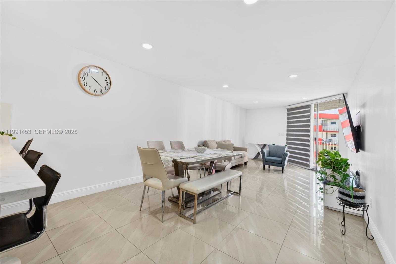 A bright, open-concept living and dining area features tile floors, a wall clock, and balcony access — 1750 W 46th St # 412, Hialeah FL 33012, HIALEAH, FL