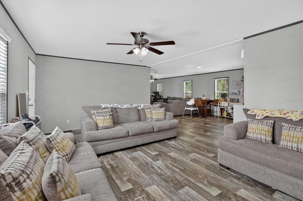 A living room features gray walls, wood-look flooring, a ceiling fan, and three gray sofas — 5139 ORLANDO AVENUE, BROOKSVILLE, FL