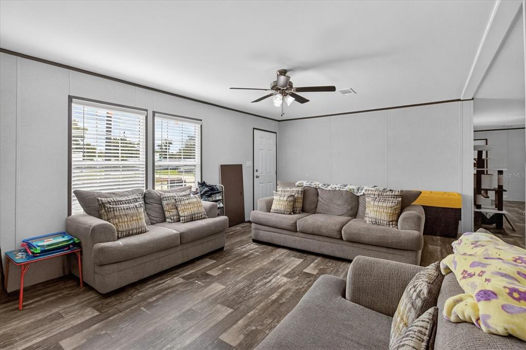 A living room features gray sofas, wood-look flooring, a ceiling fan, and two windows — 5139 ORLANDO AVENUE, BROOKSVILLE, FL