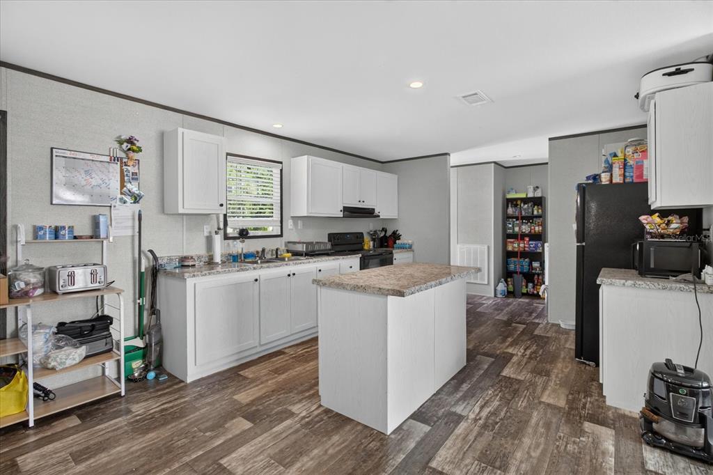 A kitchen features white cabinets, a central island, granite-look countertops, and wood-look flooring — 5139 ORLANDO AVENUE, BROOKSVILLE, FL