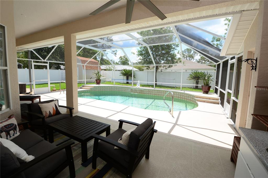 A covered patio with outdoor furniture overlooks a screened-in swimming pool in a fenced backyard — 18 WELLWATER DRIVE, PALM COAST, FL