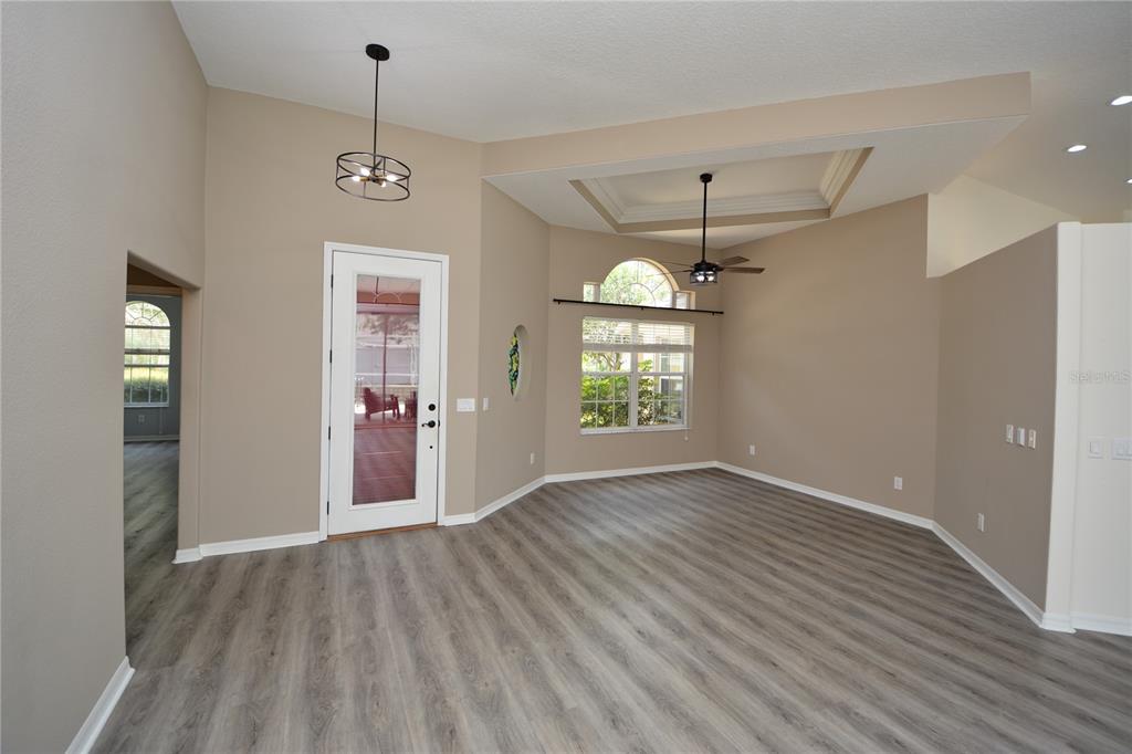 An empty living room features light gray wood-look flooring, a tray ceiling, and a glass door — 18 WELLWATER DRIVE, PALM COAST, FL