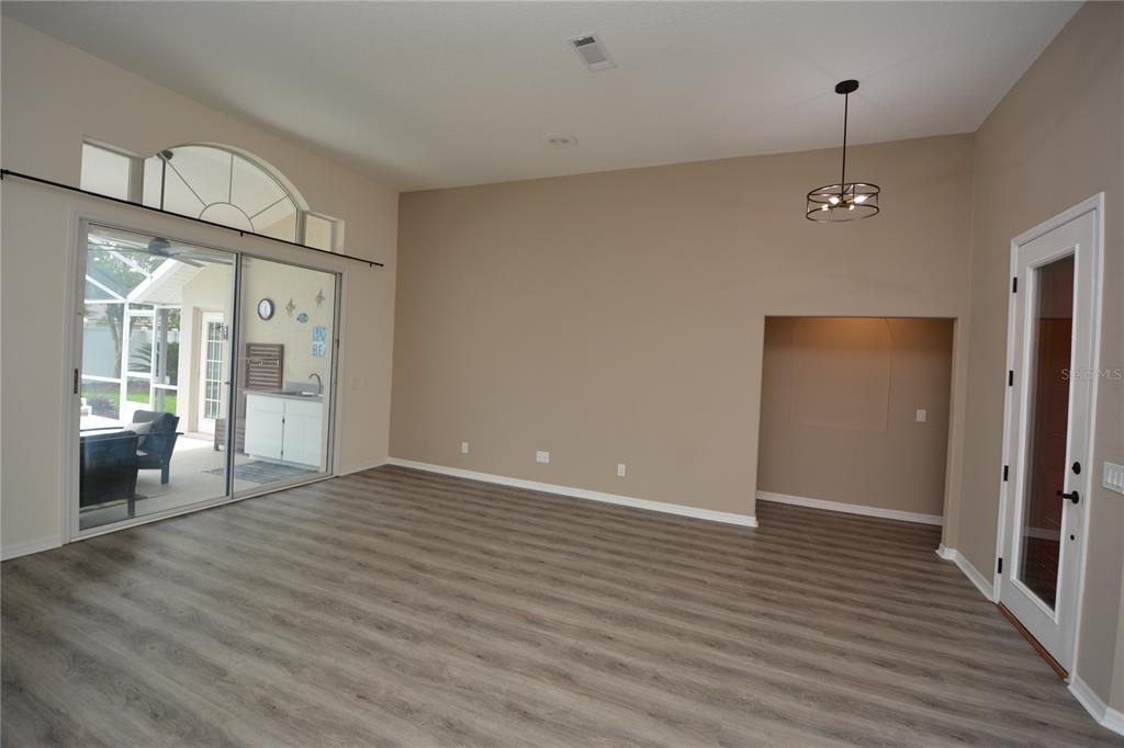 A living room with light wood-look flooring, a large sliding glass door, and a recessed alcove — 18 WELLWATER DRIVE, PALM COAST, FL