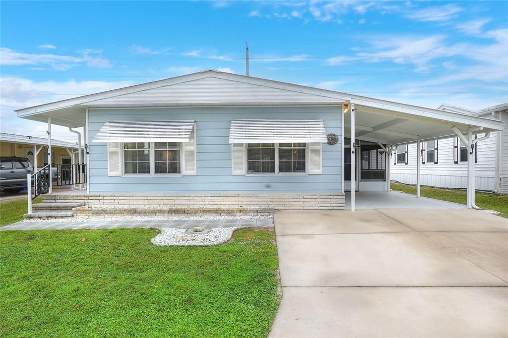 A light blue manufactured home with a white roof, carport, and a front lawn — 6308 BAYBERRY BOULEVARD NE, WINTER HAVEN, FL