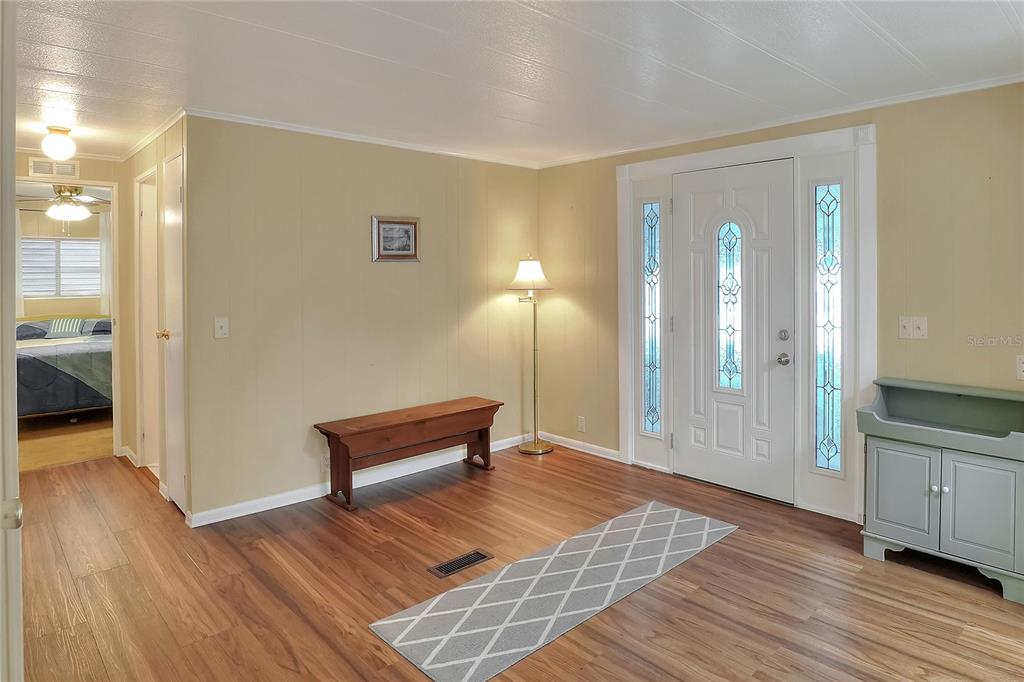 An entryway with wood-look flooring, a wooden bench, a floor lamp, and a white front door — 6308 BAYBERRY BOULEVARD NE, WINTER HAVEN, FL