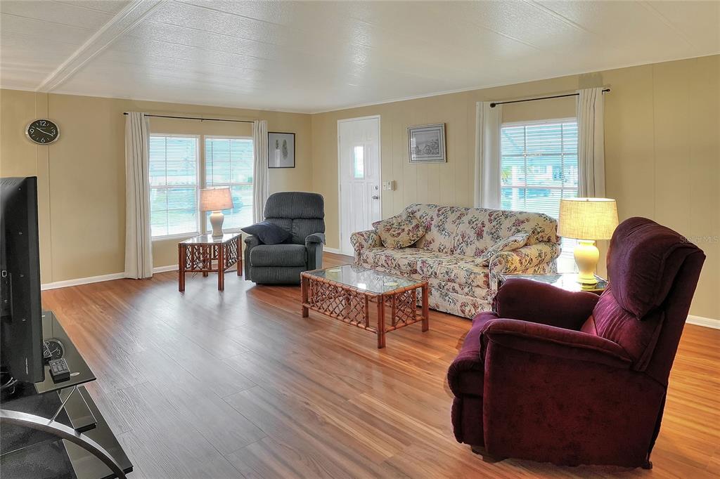 A living room features wood-look flooring, a floral sofa, two recliners, and a glass-topped coffee table — 6308 BAYBERRY BOULEVARD NE, WINTER HAVEN, FL
