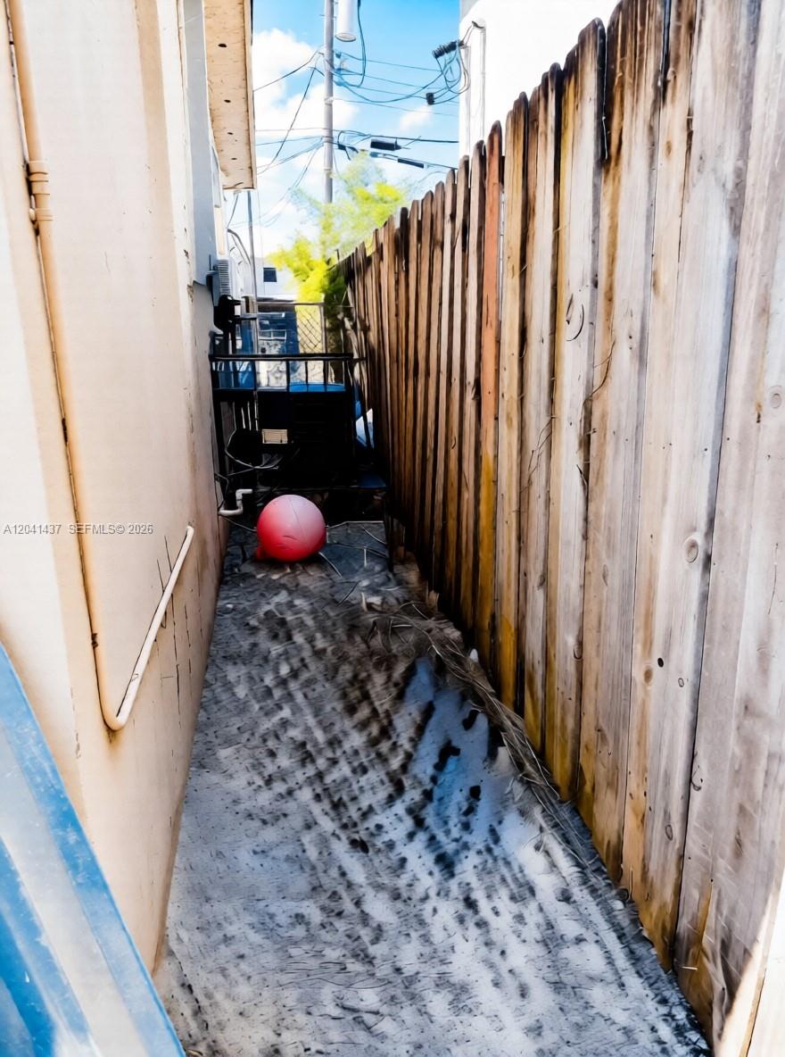 A narrow outdoor side yard features a concrete path, a wooden fence, and an air conditioner — 1896 NW 64th St # 1, Miami FL 33147, MIAMI, FL