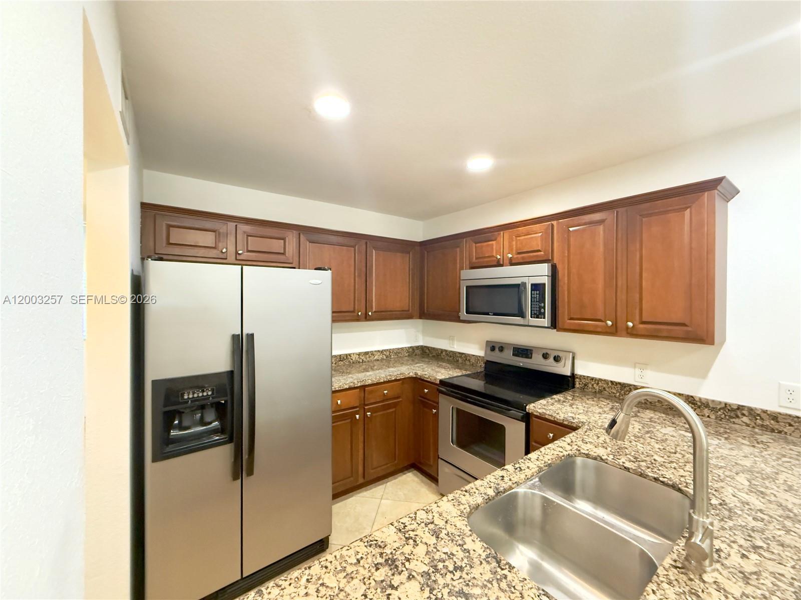 A kitchen features dark wood cabinets, granite countertops, stainless steel appliances, and tile flooring — 1000 Palm Trl # 6, Delray Beach FL 33483, DELRAY BEACH, FL
