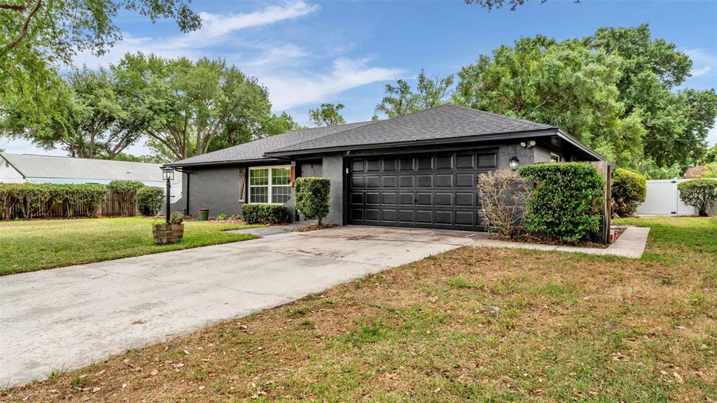 A single-story house with a dark gray exterior, black garage door, and a concrete driveway — 4301 ORANGEWOOD LOOP E, LAKELAND, FL