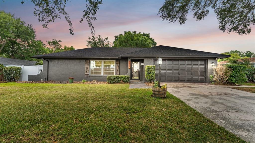 A single-story house with dark gray stucco exterior, a two-car garage, and a front lawn — 4301 ORANGEWOOD LOOP E, LAKELAND, FL