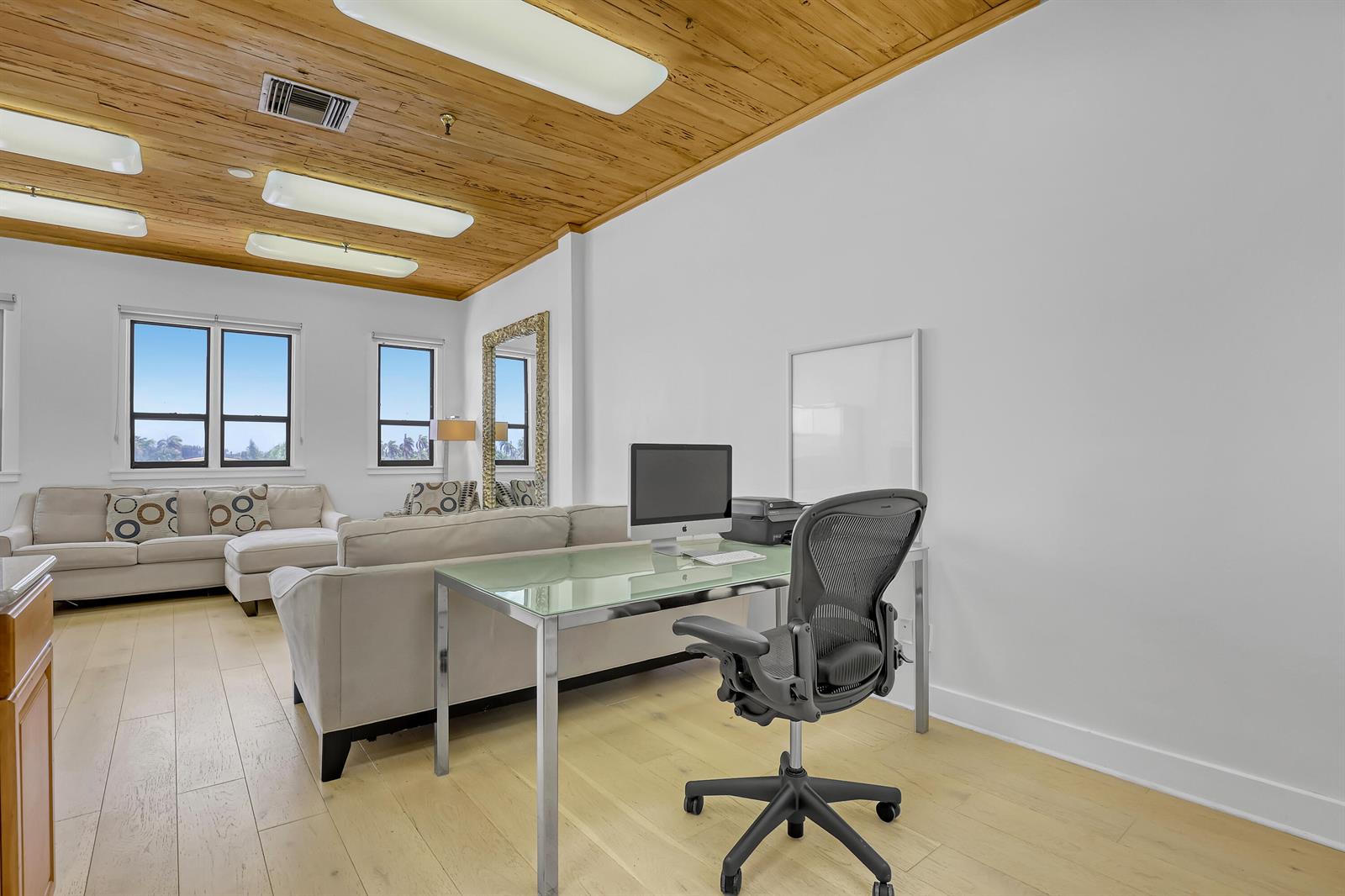 A home office area features a glass desk, ergonomic chair, and a sofa in a room with wood-paneled ceilings — 235 Sunrise Avenue, Palm Beach FL 33480, PALM BEACH, FL