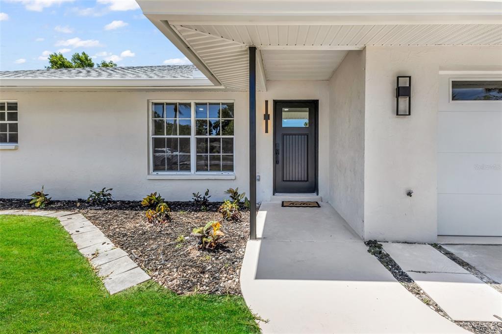 A white house exterior features a black front door, a concrete walkway, and landscaped mulch — 855 MORNINGSIDE ROAD, VENICE, FL