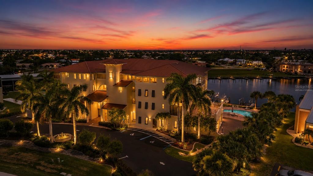An aerial view of a multi-story building with a red roof, palm trees, and pool — 1340 ROCK DOVE COURT UNIT 123, PUNTA GORDA, FL