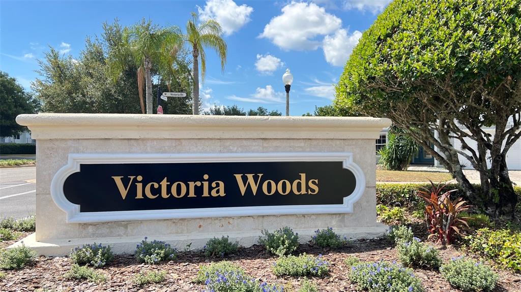 A stone monument sign with the text Victoria Woods stands in a landscaped garden area — 2353 VICTORIA DRIVE, DAVENPORT, FL