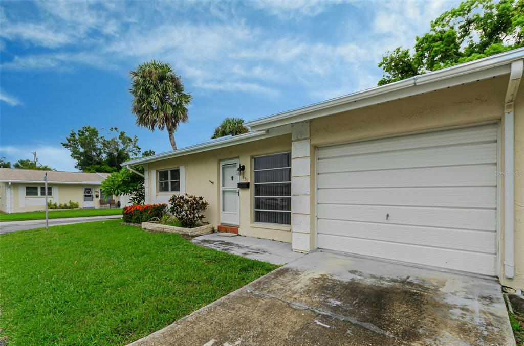 A single-story house exterior features a white garage door, a front entrance, and a grassy lawn — 830 CAMBRIDGE COURT, DUNEDIN, FL
