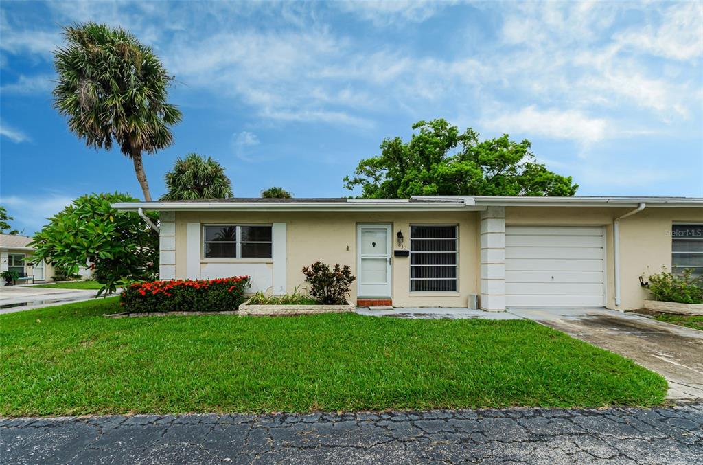 A single-story residential building features a white garage, a front door, and a grassy lawn — 830 CAMBRIDGE COURT, DUNEDIN, FL