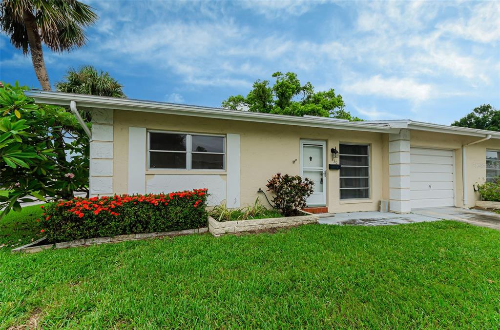 A single-story house with a beige exterior, a white garage door, and a front garden — 830 CAMBRIDGE COURT, DUNEDIN, FL