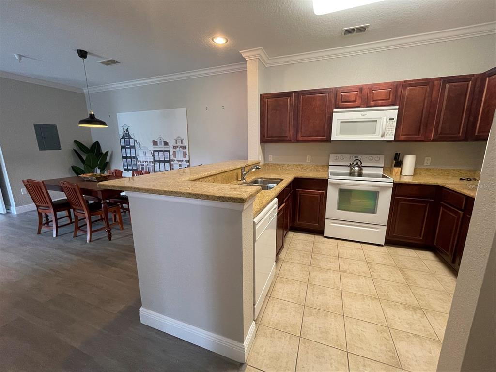 A kitchen with dark wood cabinets, granite countertops, and tile flooring opens to a dining area — 1370 TUSCAN TERRACE UNIT 2307, DAVENPORT, FL