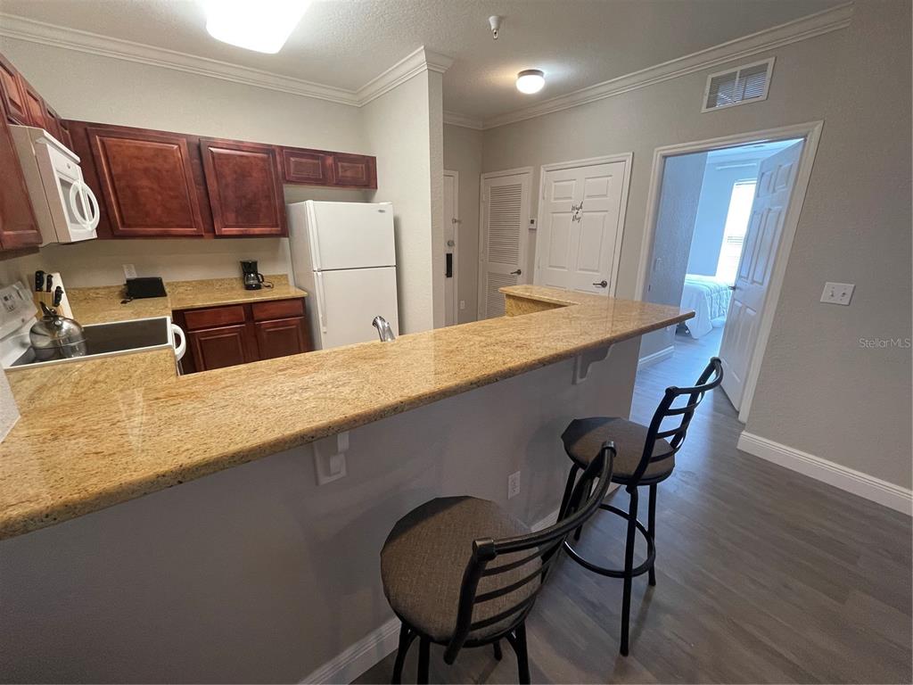A kitchen features dark wood cabinets, granite countertops, a white refrigerator, and two bar stools — 1370 TUSCAN TERRACE UNIT 2307, DAVENPORT, FL