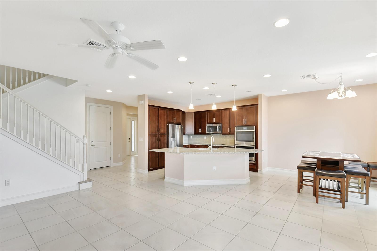 A kitchen with dark wood cabinets, a granite island, and tile flooring next to stairs — 10102 Akenside Drive, Boca Raton FL 33428, BOCA RATON, FL
