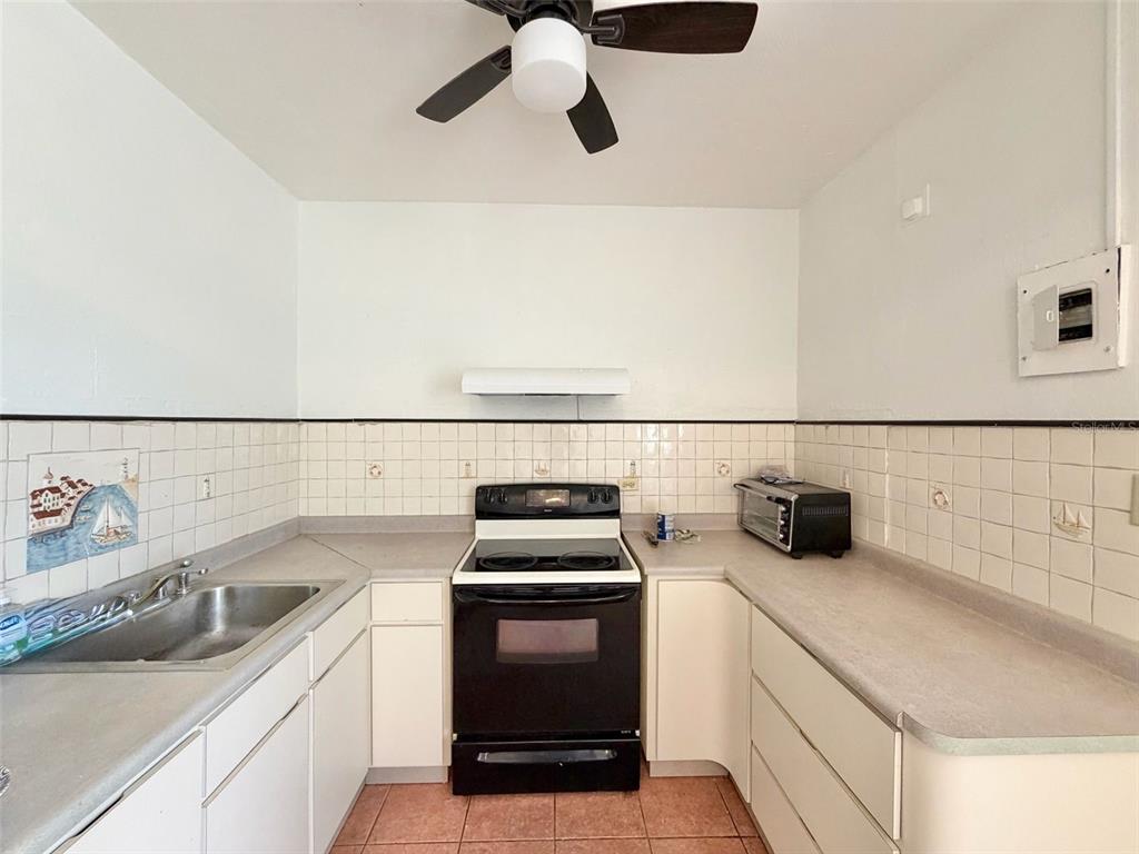 A kitchen features white cabinets, a black stove, a stainless steel sink, and tiled walls — 139 L STREET RAMEY BASE, AGUADILLA, PR