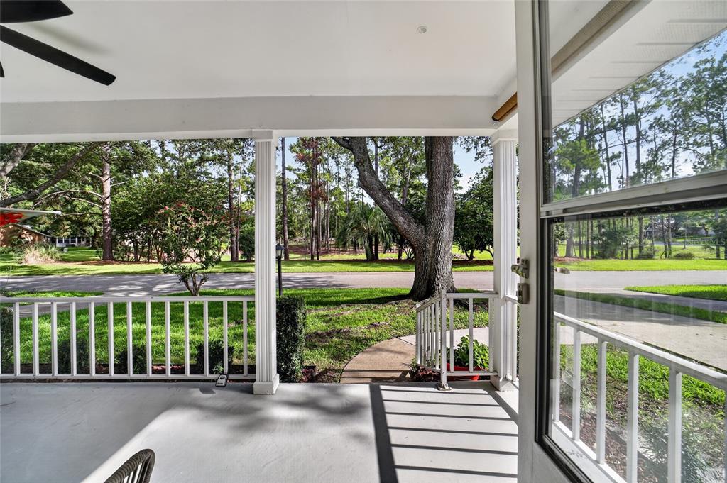 A covered porch with white railings overlooks a grassy yard with trees and a street — 8891 SW 96TH LANE UNIT E, OCALA, FL