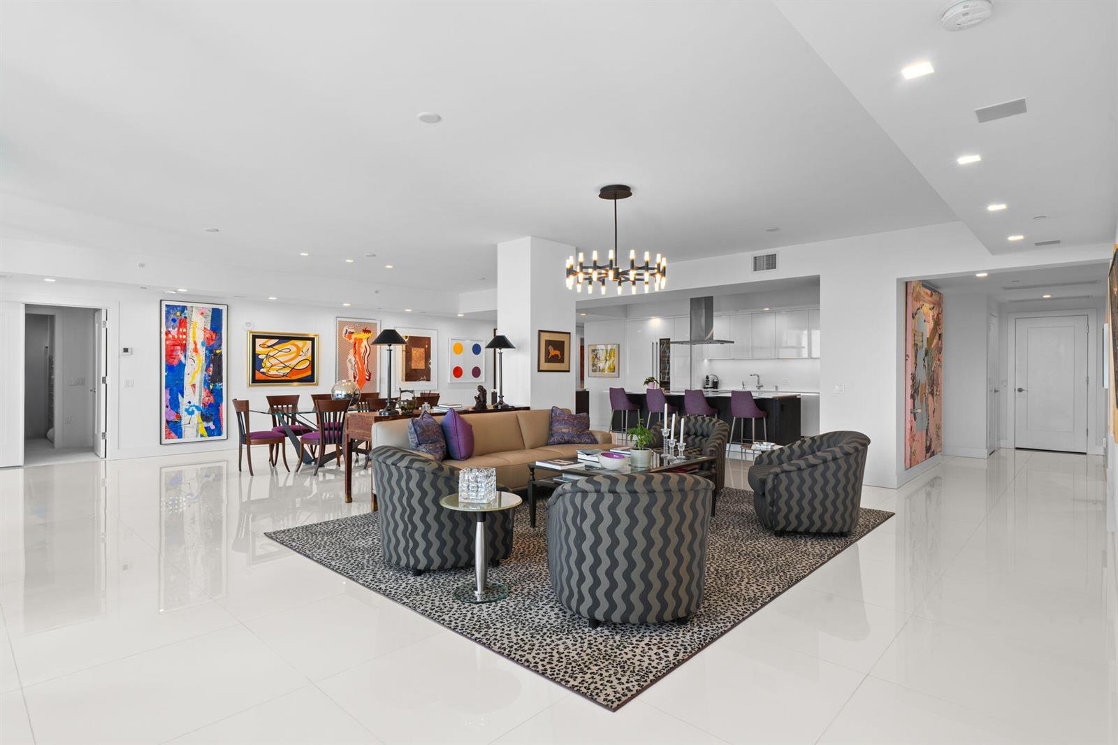 A modern, open-concept living and dining area features white tile floors and colorful abstract art — 20155 Boca West Drive # A404, Boca Raton FL 33434, BOCA RATON, FL