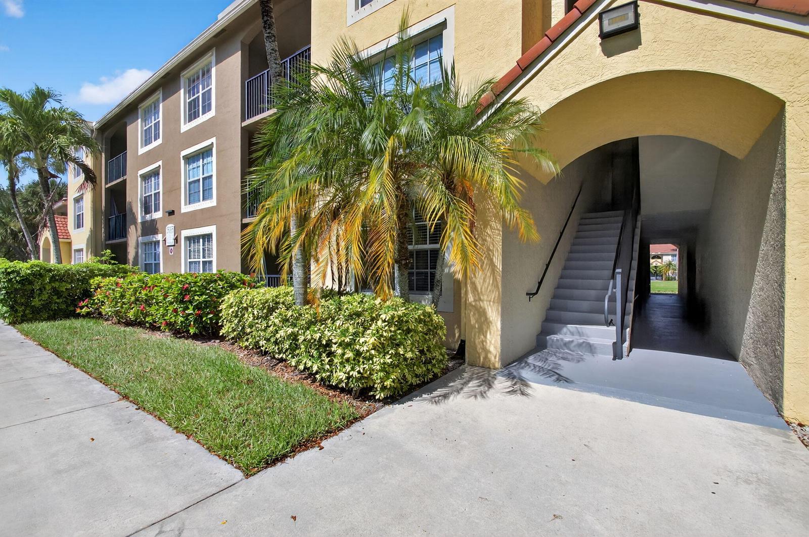 An exterior view of a multi-story apartment building with stairs leading to an arched entrance — 15035 Michelangelo Boulevard # 105, Delray Beach FL 33446, DELRAY BEACH, FL