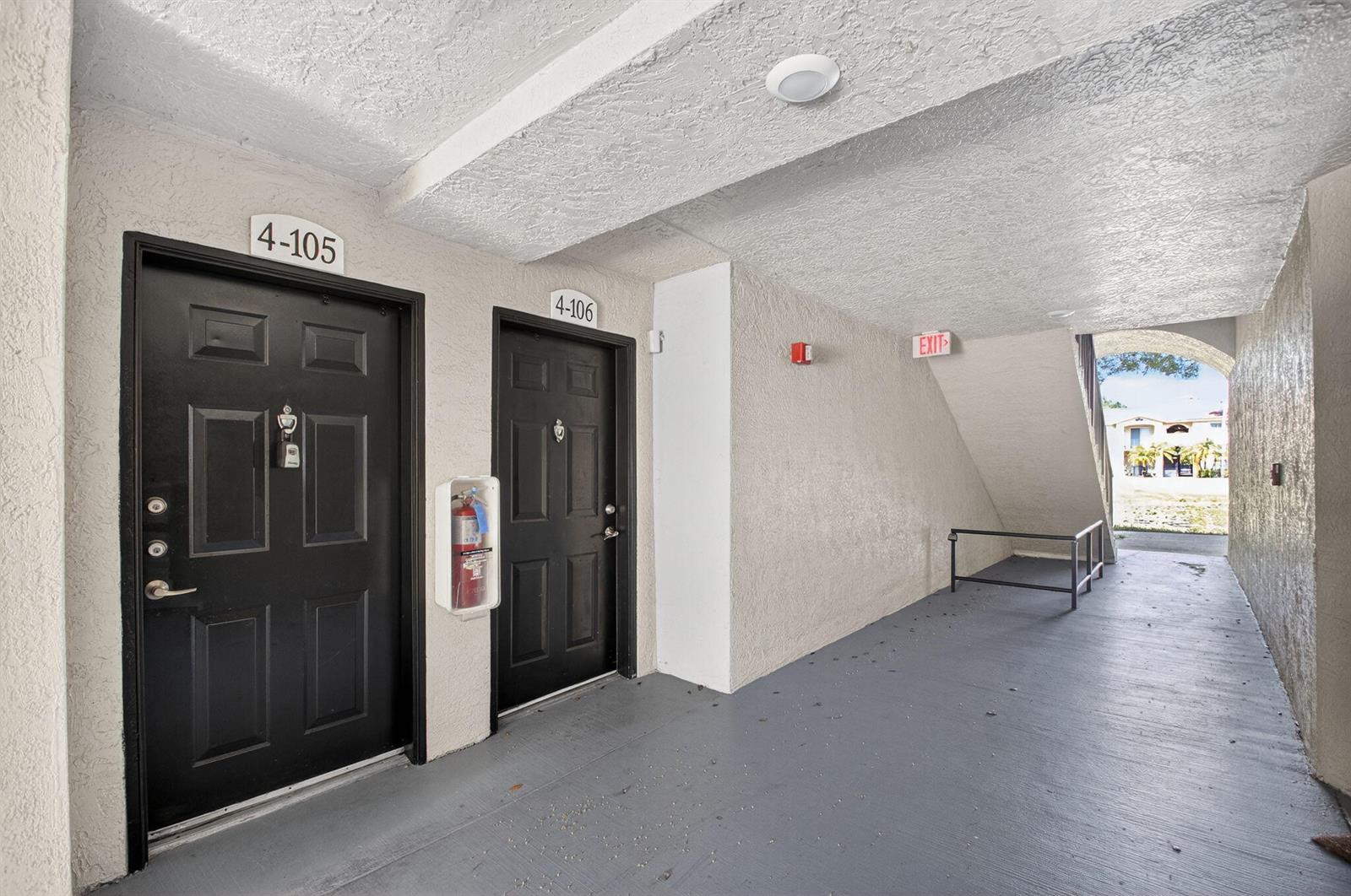 An outdoor apartment hallway features two black doors labeled 4-105 and 4-106 with a fire extinguisher — 15035 Michelangelo Boulevard # 105, Delray Beach FL 33446, DELRAY BEACH, FL