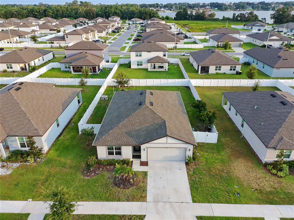 An aerial view shows a suburban neighborhood with single-family homes and white vinyl fences — 1067 MICHELANGELO LANE, WINTER HAVEN, FL