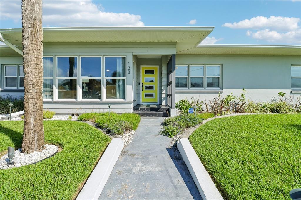 A single-story house with a light green exterior, a bright yellow front door, and a walkway — 133 PARK AVENUE, DAYTONA BEACH, FL
