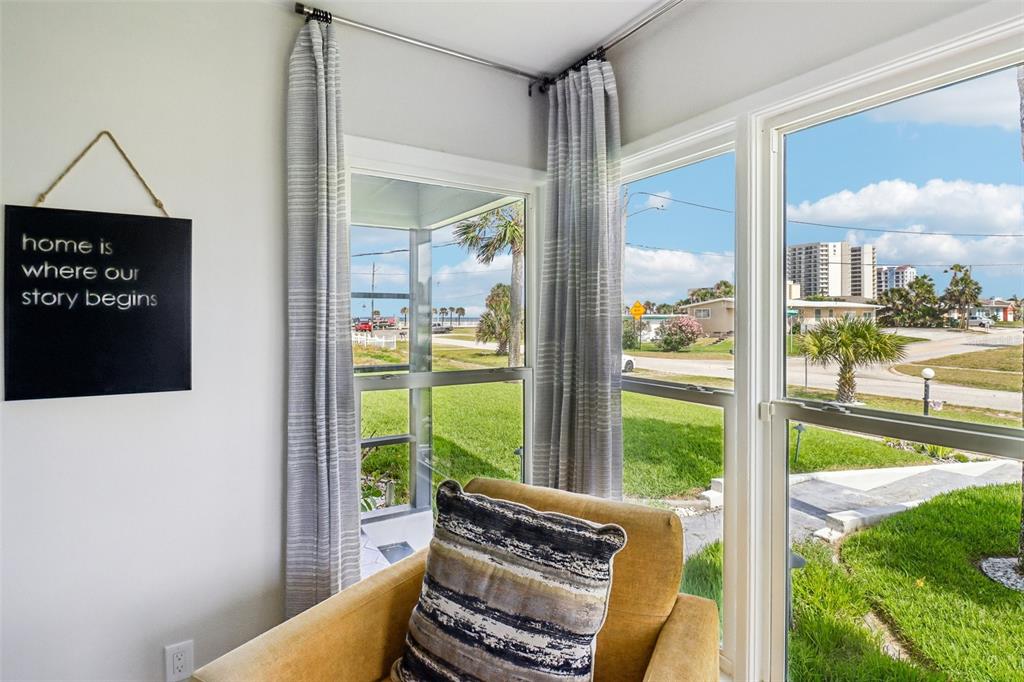 A yellow armchair sits in a corner room with large windows overlooking a coastal street — 133 PARK AVENUE, DAYTONA BEACH, FL