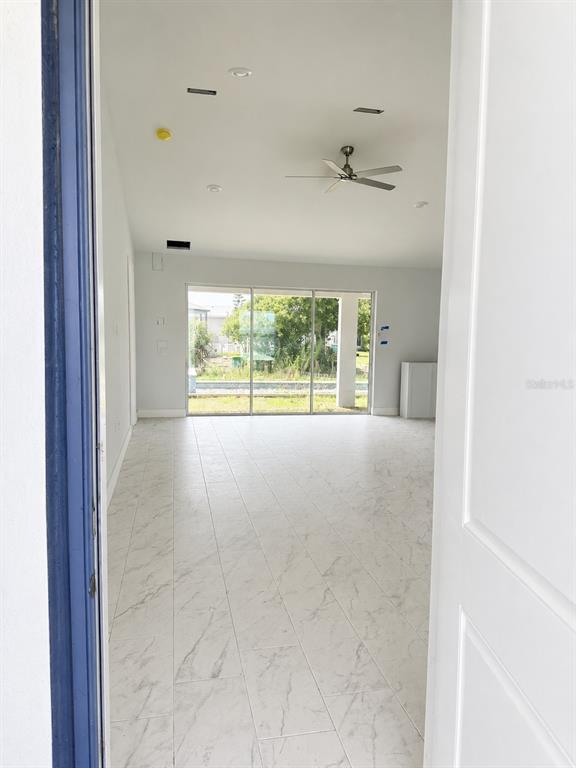 An interior view of an open-concept room with white marble-look tile flooring and sliding doors — 9057 BANTRY BAY BOULEVARD, ENGLEWOOD, FL