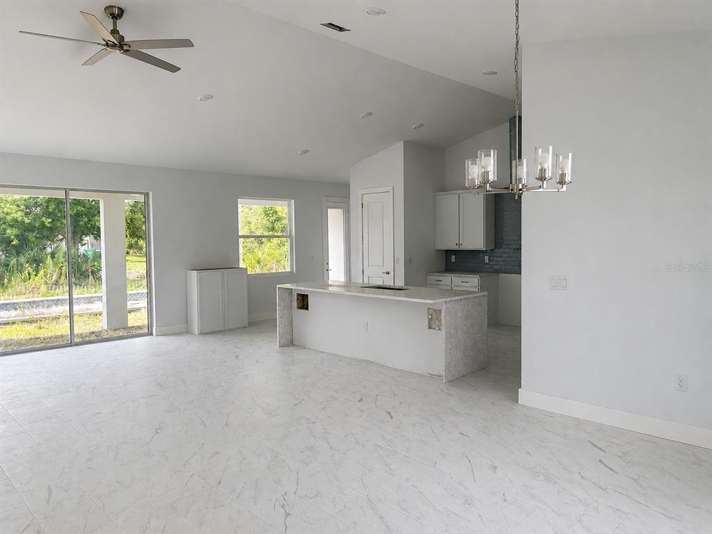 An open-concept kitchen and living area featuring white cabinetry, a stone island, and tile flooring — 9057 BANTRY BAY BOULEVARD, ENGLEWOOD, FL