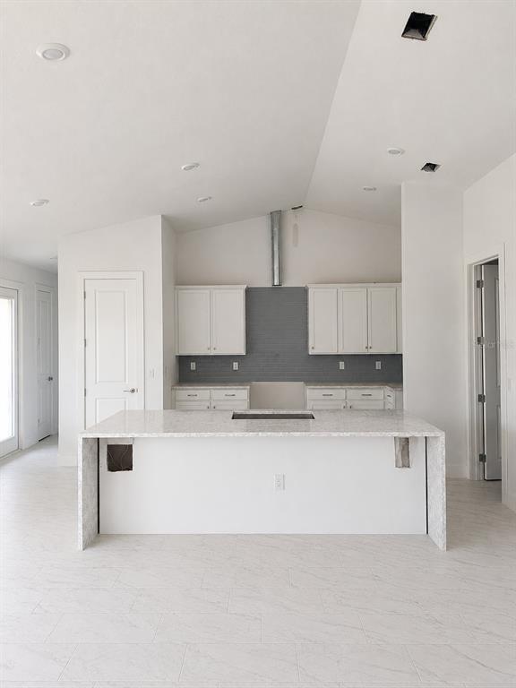 A modern kitchen features white cabinets, a gray tiled backsplash, and a large marble-topped island — 9057 BANTRY BAY BOULEVARD, ENGLEWOOD, FL