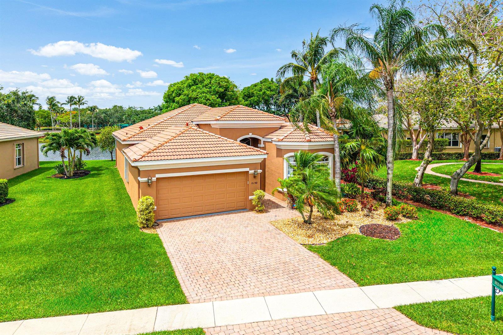 A tan single-story house with a tile roof, brick driveway, and palm trees on a lawn — 8240 Parini Way, Lake Worth FL 33467, LAKE WORTH, FL