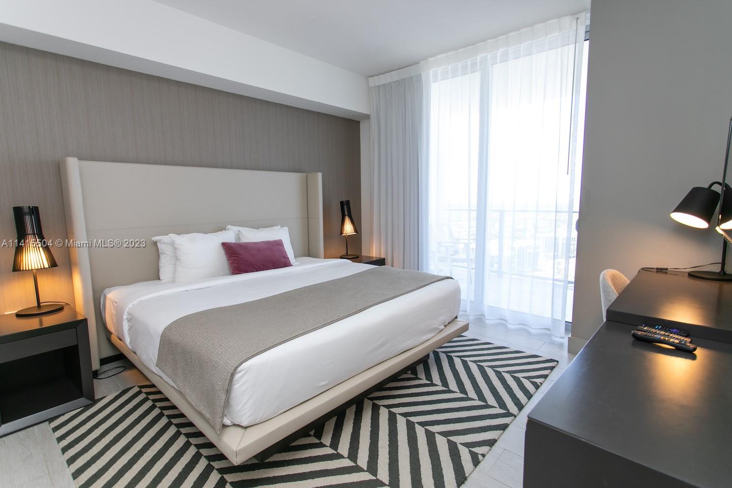 A modern bedroom features a king bed, patterned area rug, desk, and floor-to-ceiling windows — 4010 S Ocean Dr # 1201, Hollywood FL 33019, HOLLYWOOD, FL