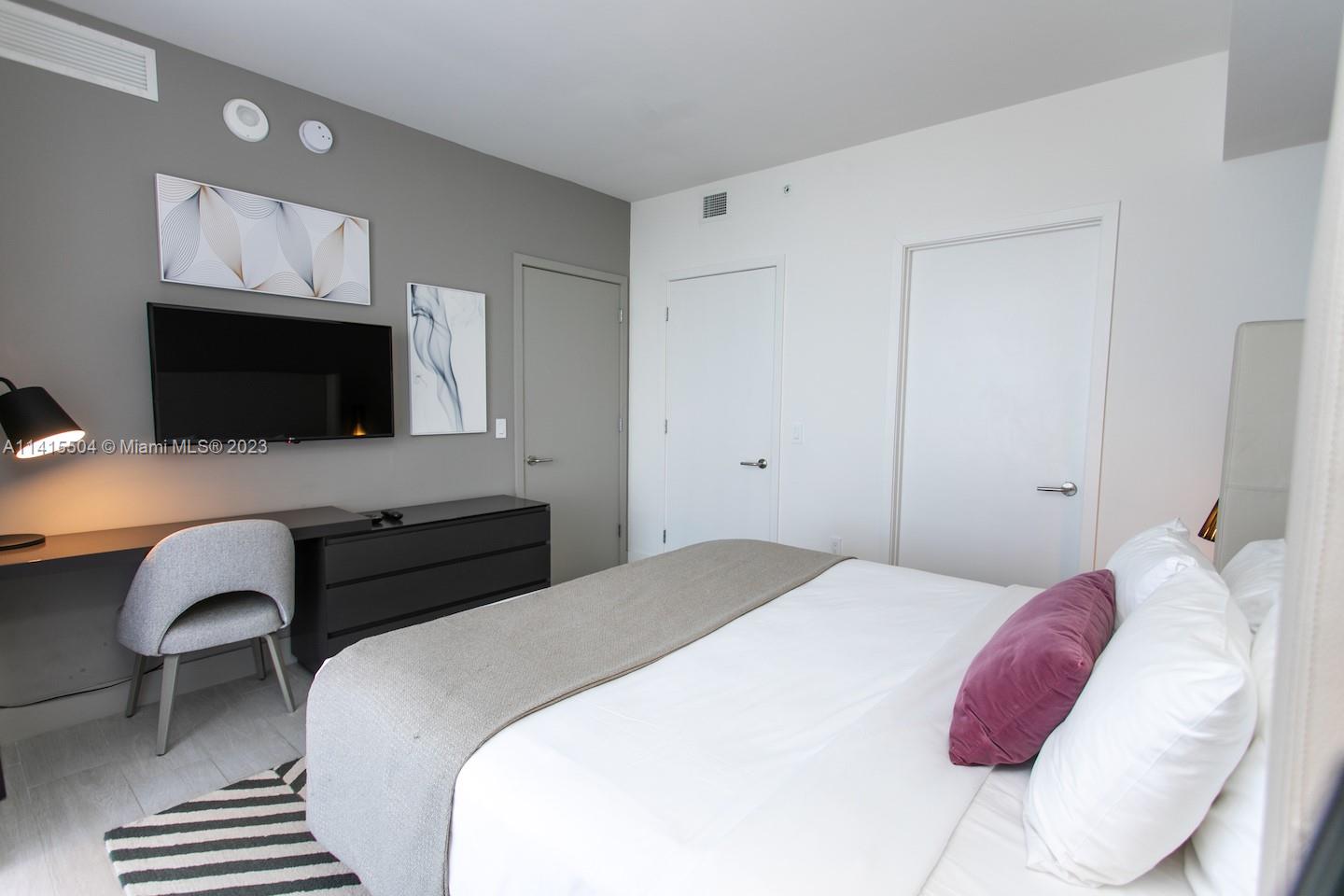 A bedroom features a bed, a desk with a chair, a television, and three doors — 4010 S Ocean Dr # 1201, Hollywood FL 33019, HOLLYWOOD, FL