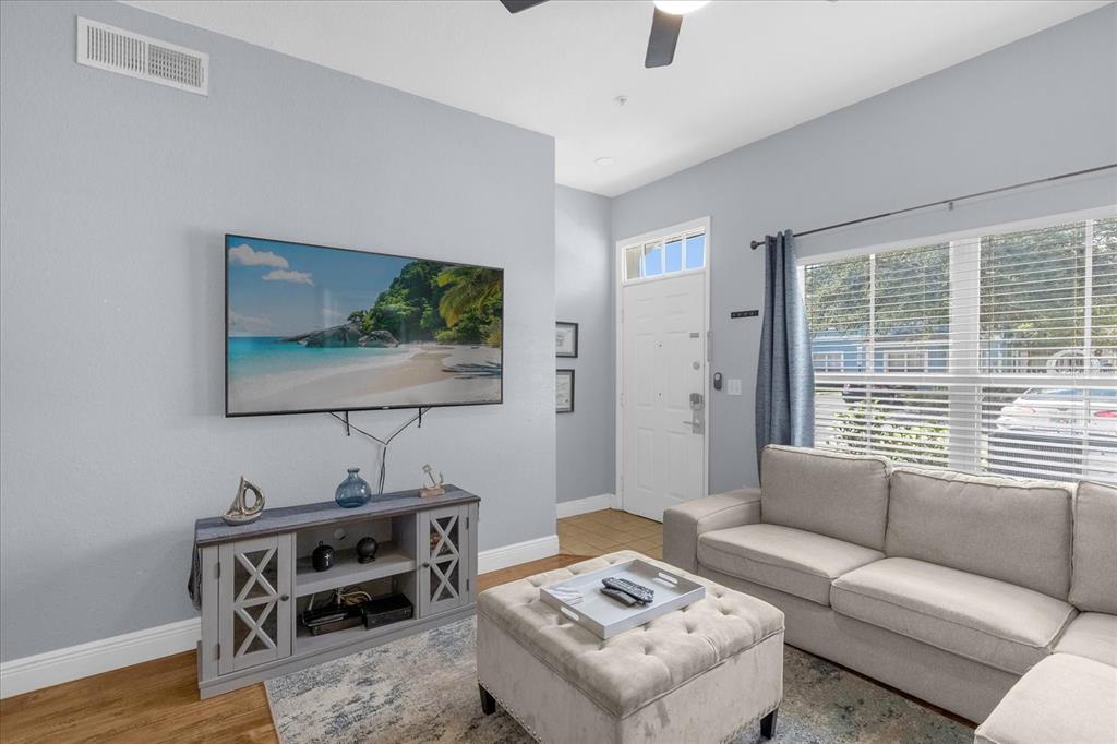 A living room features a wall-mounted television, a grey media console, and a sectional sofa — 2213 SAN VITTORINO CIRCLE UNIT 106, KISSIMMEE, FL