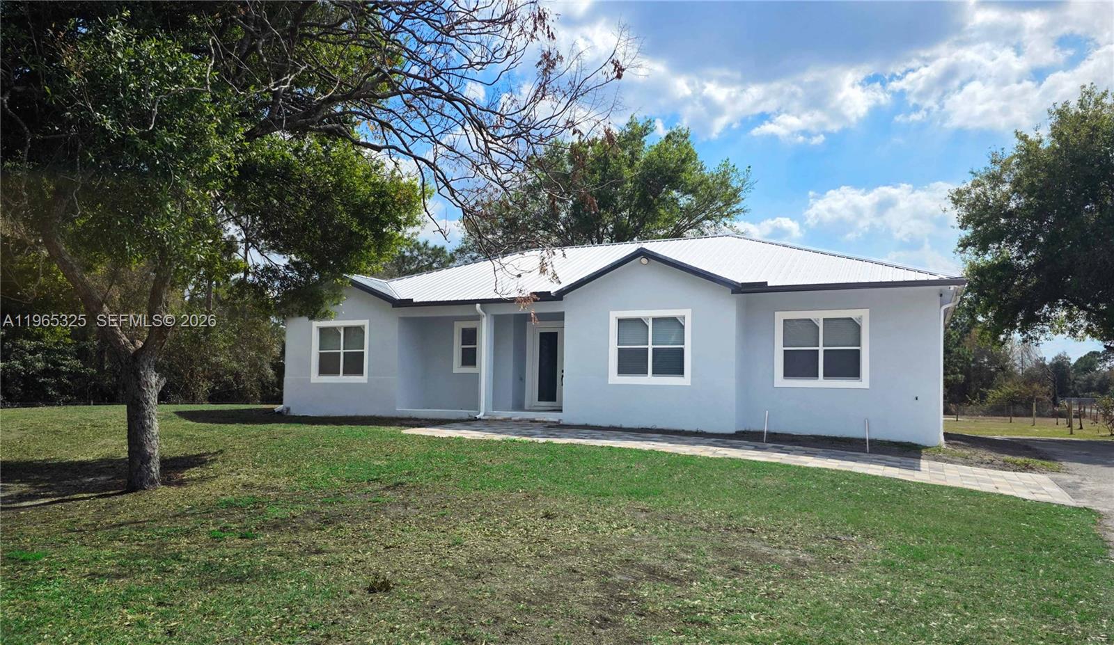 A single-story light gray house with a metal roof sits on a grassy lot — 548 Bald Cypress Ave, Clewiston FL 33440, CLEWISTON, FL