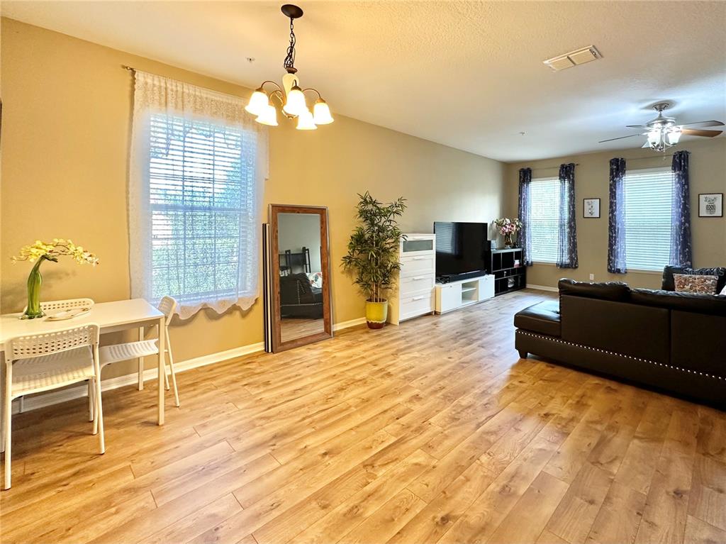 A living and dining area with light wood flooring, a dark sofa, and a television — 4309 REGAL TOWN LANE, LAKE MARY, FL