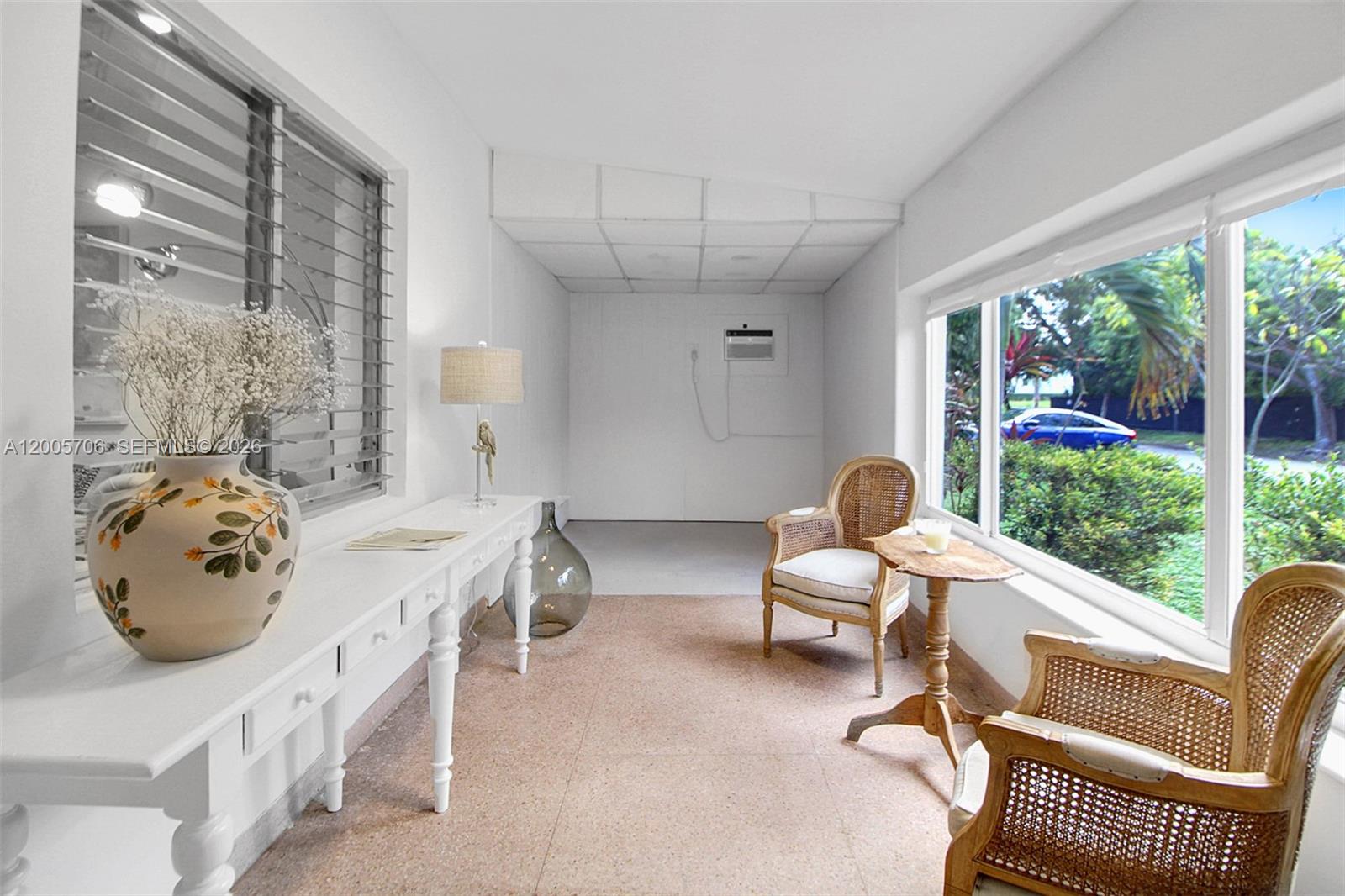 A sunroom features a white console table, two wicker chairs, and large windows overlooking greenery — 231 NE 43rd St, Miami FL 33137, MIAMI, FL